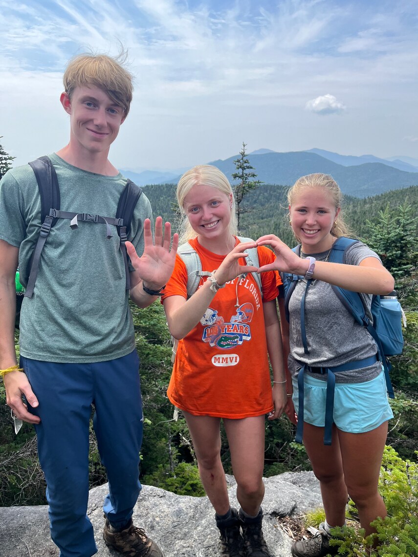 Campers smiling on mountain making a heart out of their hands